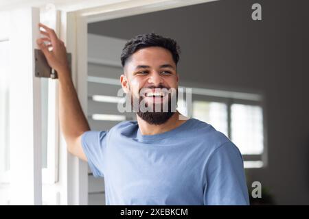 Smiling man standing at home, looking outside through open door Stock Photo