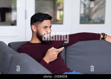 Relaxing on couch, man smiling while using smartphone at home Stock Photo