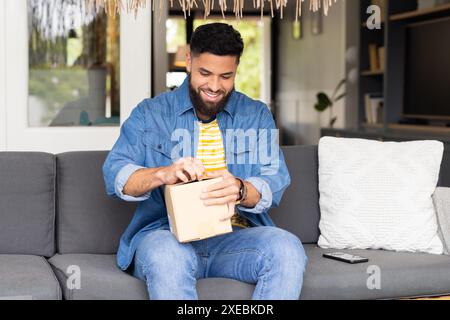 Man opening package while sitting on couch at home, smiling happily Stock Photo