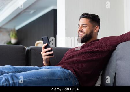 Relaxing on couch, man smiling while using smartphone at home Stock Photo