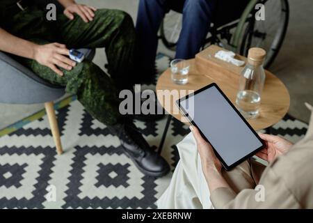 High angle closeup of unrecognizable woman holding digital tablet with blank white screen while consulting two army veterans in session copy space Stock Photo