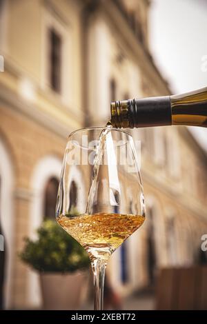 Glass of white wine is being poured on a wooden table of an outdoor restaurant Stock Photo