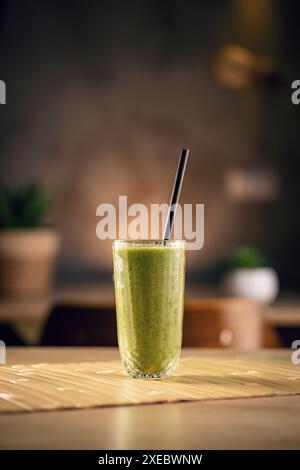 Green smoothie standing on bamboo mat with straw in modern kitchen Stock Photo