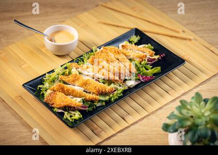 Breaded chicken strips are served on a bed of lettuce with a side of dipping sauce Stock Photo