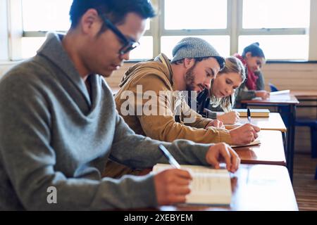 College students, writing and desk in classroom with books for english literature or language for exam. People, university and scholarship for Stock Photo
