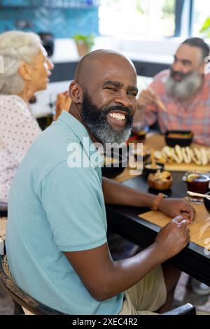 At home, Smiling man enjoying meal with senior friends at dining table, having good time Stock Photo