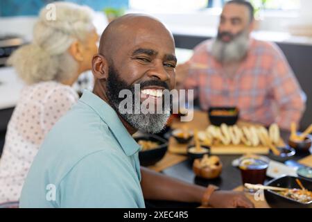 At home, Smiling man enjoying meal with senior friends at dining table, having fun Stock Photo