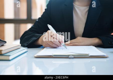 A woman in a suit is writing with a pen on a piece of paper Stock Photo