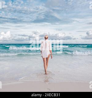 Woman wearing white loose tunic over bikini on Mahe Island, Seychelles. Summer vacations on picture perfect tropical beach concept. Stock Photo