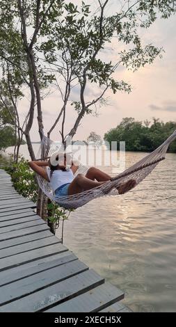 A woman relaxes in a hammock on a dock, enjoying the peaceful waters and gentle breeze on a sunny day Stock Photo