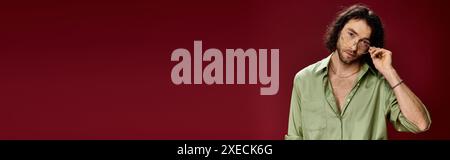 Handsome man in green silk shirt and glasses posing against red background. Stock Photo