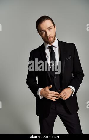 A stylish gentleman in a suit and tie confidently poses for a portrait in a studio setting against a grey background. Stock Photo