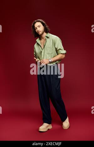 Handsome man in glasses and green silk shirt posing confidently on red background. Stock Photo