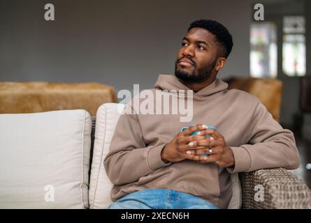 Joyful young man  having a coffee or tea, resting, sitting on the sofa in the living room at home. Lifestyle photos  of real people Stock Photo