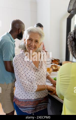 At home, Smiling senior woman preparing food with friends in kitchen, enjoying time together Stock Photo