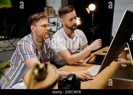 Two men engrossed in work on a laptop at a desk. Stock Photo