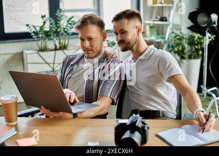 Two men in stylish attire engrossed in work on a laptop at a table. Stock Photo