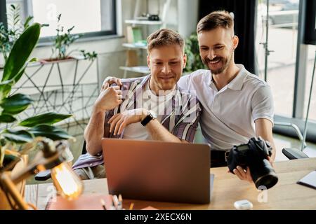 Two men in casual clothing sitting at a table, engrossed in using a laptop. Stock Photo