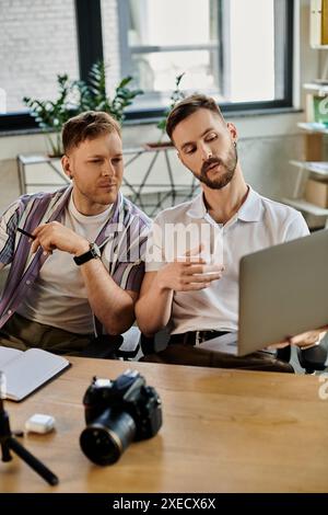 Two men in casual attire engrossed in laptop work together at a table. Stock Photo