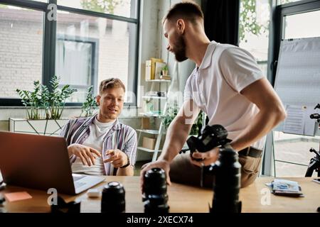 Two men wearing comfy attires sitting at a table, working on a laptop together. Stock Photo