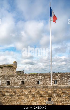The French flag waving at Port Louis Citadelle in Lorient, Brittany, France. A historical fort with a scenic view and cloudy sky. Stock Photo