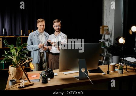 Two happy men, stylishly dressed, collaborate on a computer at a desk. Stock Photo