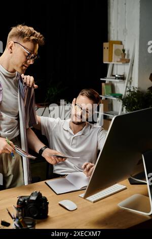 Two men in casual attire sit at a desk, engrossed in the laptop screen. Stock Photo