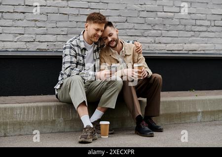 Two young men in casual attire sit, engrossed in a cell phone. Stock Photo