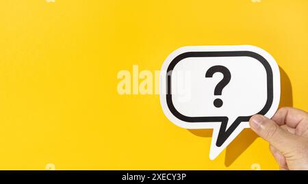 Hand holding a question mark on speech bubble on yellow background. Copy space Stock Photo