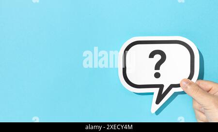 Hand holding a question mark on speech bubble on blue background. Copy space Stock Photo