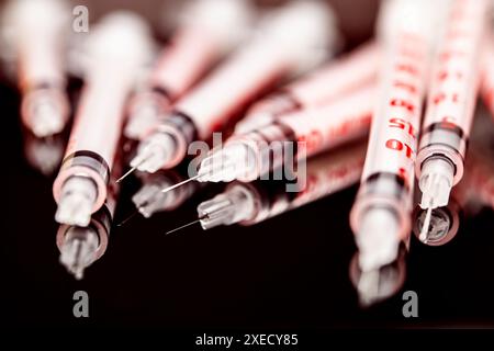 This photograph captures an array of medical insulin syringes closely packed together on a dark, reflective surface, highlighting their sharp needles Stock Photo