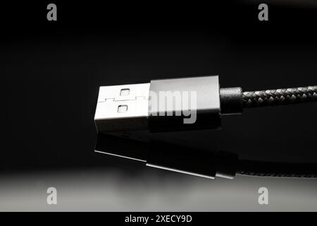 Close-up view of a USB connector with braided cable design on a reflective black surface, highlighting modern connectivity solutions. Stock Photo