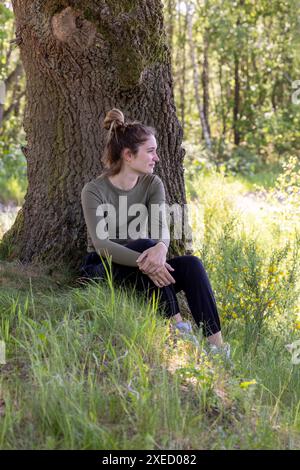 Thoughtful Woman Sitting by an Old Tree in a Lush Forest Stock Photo