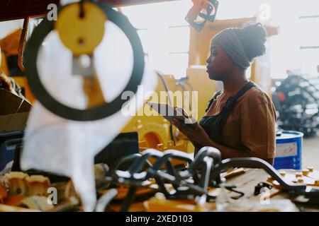 Young African American factory worker checking industrial machine and using digital tablet Stock Photo