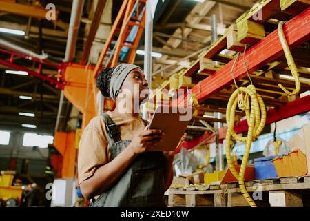 Low angle view of young African American female factory worker holding digital tablet doing inventory, copy space Stock Photo