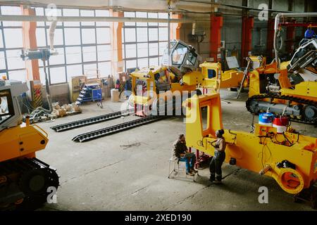 High angle view extreme long shot of biracial male and female specialists working at modern bulldozer production factory, copy space Stock Photo