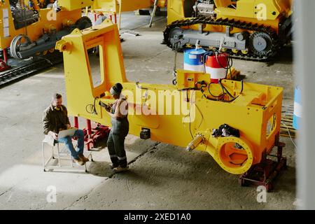 High angle view of two biracial coworkers sitting and standing by part of bulldozer machine using laptop and digital tablet Stock Photo