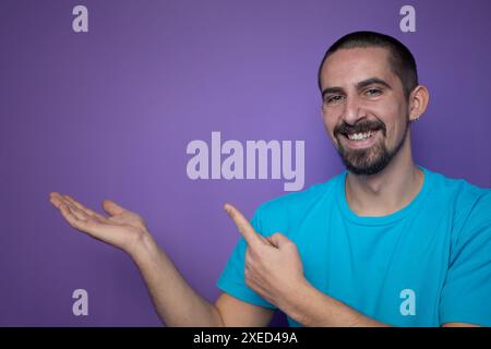 Young man pointing empty space using hands and fingers, isolated over violet background Stock Photo
