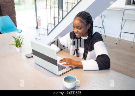 Joyful Remote Work: Young Woman Typing on Laptop in Bright Modern Home Stock Photo