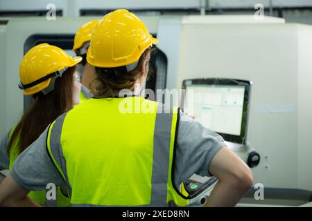 Back view of group young factory worker wearing a hard hat looking at a computer screen used to control production. Stock Photo
