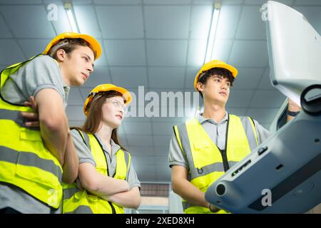 Both of  young factory worker wearing a hard hat looking at a computer screen used to control production. Stock Photo