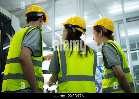 Back view of group young factory worker wearing a hard hat looking at a computer screen used to control production. Stock Photo