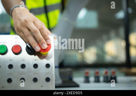 Close-up of hand pressing the stop button on the control panel of an industrial machine. Stock Photo