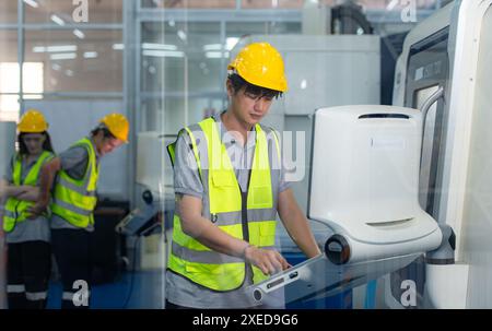 Portrait of young male factory worker wearing a hard hat looking at a computer screen used to control production. Stock Photo