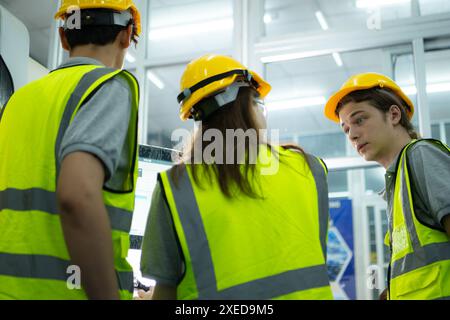 Back view of group young factory worker wearing a hard hat looking at a computer screen used to control production. Stock Photo
