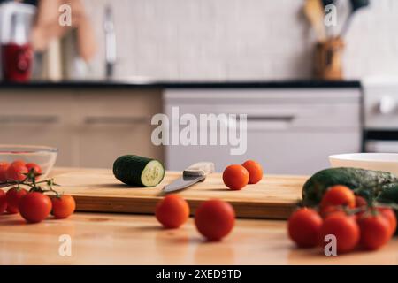 Slicing cherry tomatoes and cucumbers on a wooden table on a kitchen background Stock Photo