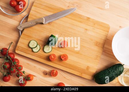 Slicing cherry tomatoes and cucumbers on a wooden table Stock Photo