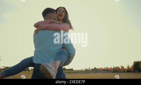 Happy Caucasian loving family couple woman female man male having fun boyfriend girlfriend hugging cuddle spinning around outside meadow countryside Stock Photo