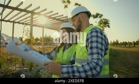 Female male workers Caucasian woman man builders girl guy engineers discussing installation talking environmental plan technicians analyzing blueprint Stock Photo