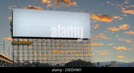A large white billboard on scaffolding in front of a sunset sky. The billboard is blank. The sky is a deep orange, with a few wispy clouds. The sun is Stock Photo